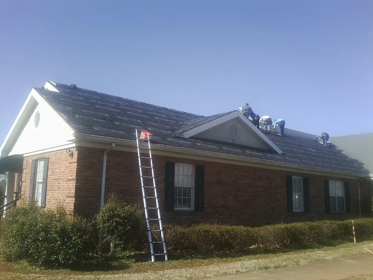 Crew tearing shingles off a brick ranch roof with a ladder set — Emergency Roof Repair work by our crew in Boothville