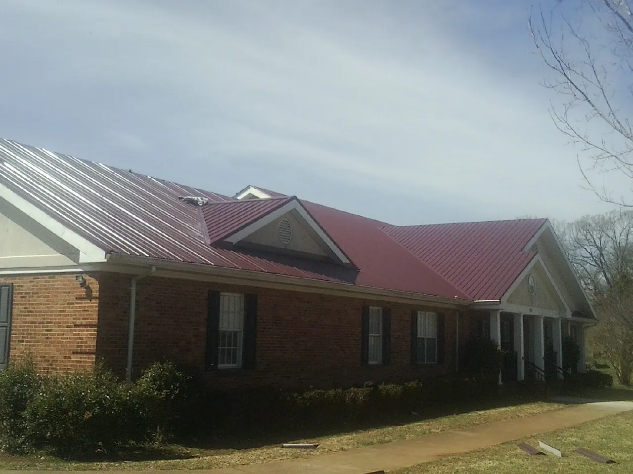 Red metal roof with gabled entries on a long brick building, from a Hail Damage Roof Repair job in Boothville