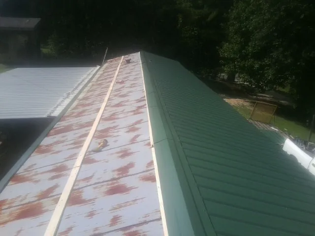 Old rusted panels beside newly installed green metal roofing — Wind Damage Roof Repair by Roofing Brothers in Boothville