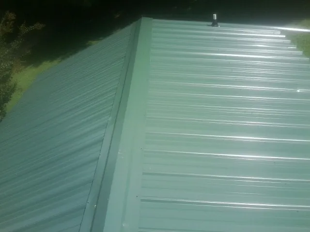New green metal panels meeting at the ridge of a roof — Flat Roof Repair work by our crew in Boothville
