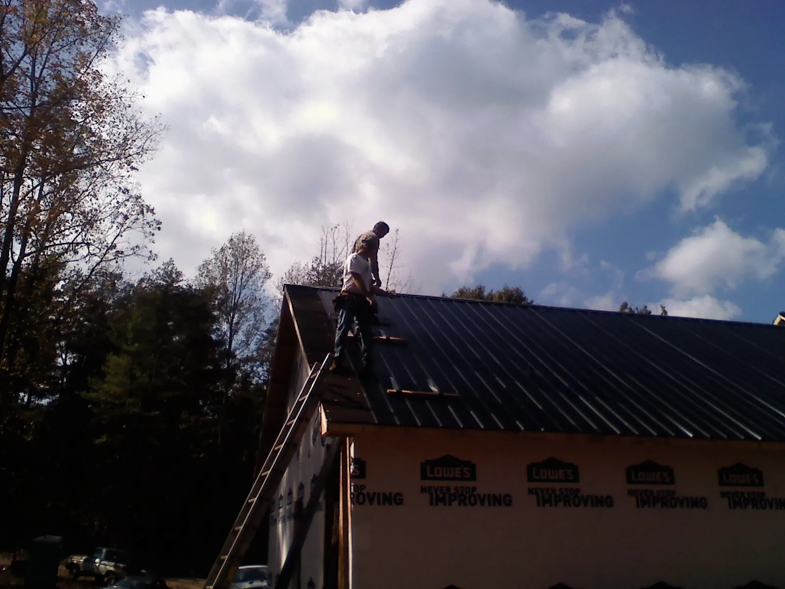 Roofer fastening dark metal panels high against a cloudy sky, from a Roof Inspection job in Boothville