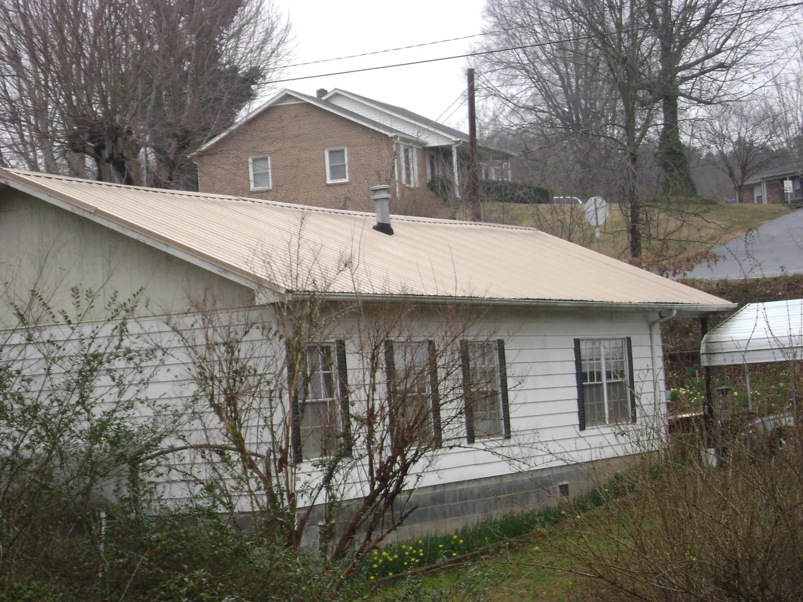 Tan metal roof on a white sided house set into a hillside — Commercial Roofing by Roofing Brothers in Boothville
