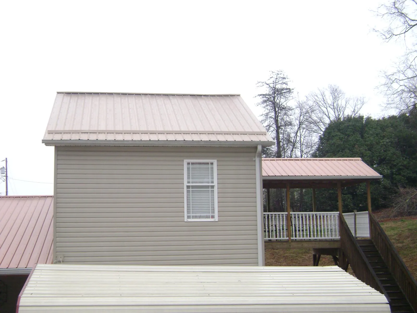 Tan metal roofs on a two story addition and attached porch, from a Roof Replacement job in Boothville